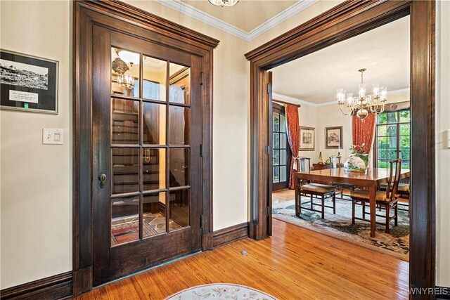 doorway featuring baseboards, wood finished floors, a notable chandelier, and ornamental molding