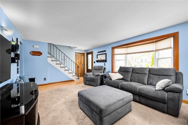carpeted living area with baseboards and stairs