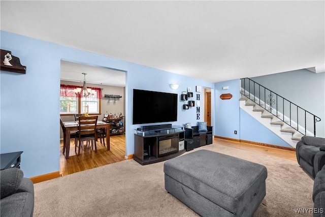 carpeted living room featuring stairway, baseboards, and a notable chandelier