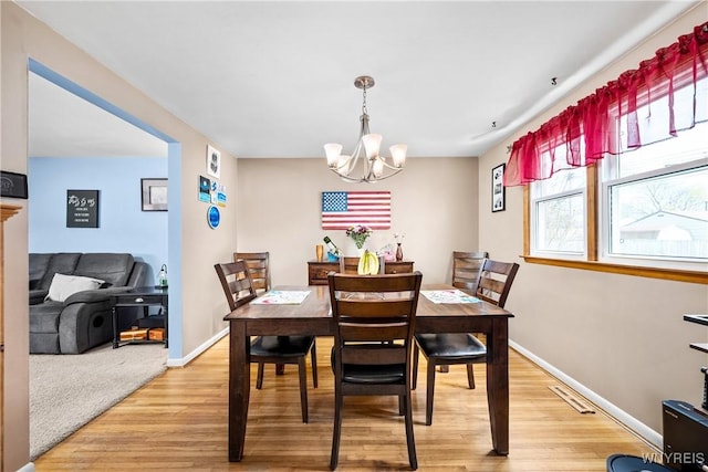 dining space with light wood finished floors, baseboards, visible vents, and a chandelier