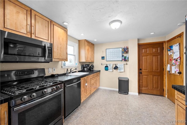 kitchen with recessed lighting, dark countertops, a sink, baseboards, and appliances with stainless steel finishes