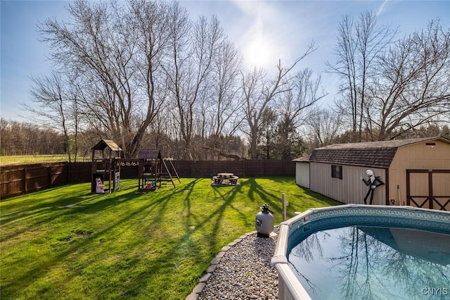 view of swimming pool with a fenced backyard, an outbuilding, a playground, and a lawn