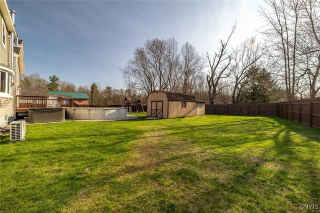 view of yard with a fenced in pool, a fenced backyard, a shed, a wooden deck, and an outbuilding