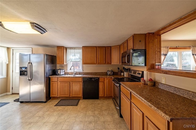 kitchen with brown cabinetry, a sink, dark countertops, and appliances with stainless steel finishes