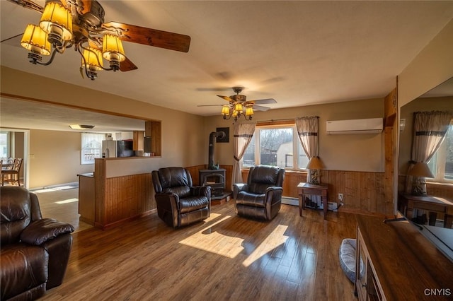 living area with a wall mounted air conditioner, a wood stove, wood finished floors, and a wainscoted wall