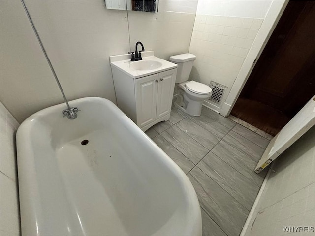 bathroom with vanity, tile walls, a freestanding bath, toilet, and visible vents