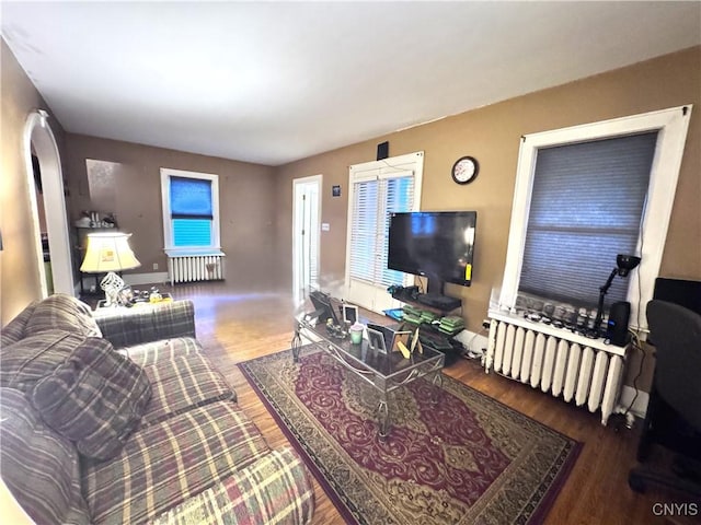 living area with arched walkways, radiator heating unit, and wood finished floors