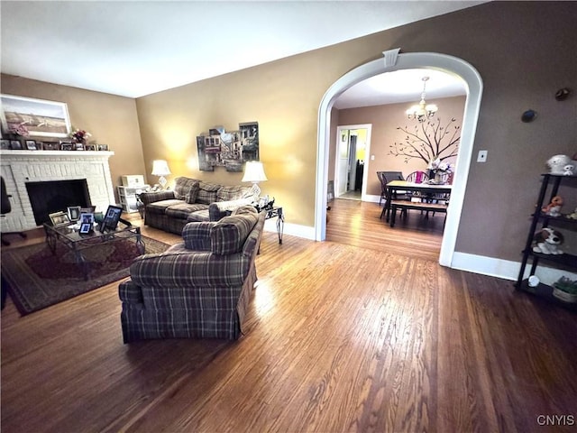 living area with an inviting chandelier, wood finished floors, arched walkways, baseboards, and a fireplace