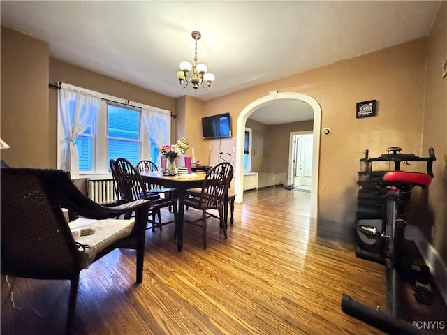 dining area featuring an inviting chandelier, wood finished floors, and arched walkways