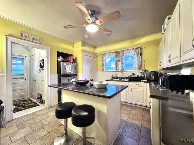 kitchen with dark countertops, black microwave, a breakfast bar, ceiling fan, and white cabinetry