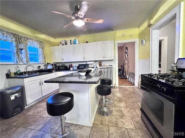 kitchen featuring a sink, stainless steel gas range, a center island, a kitchen bar, and white cabinetry