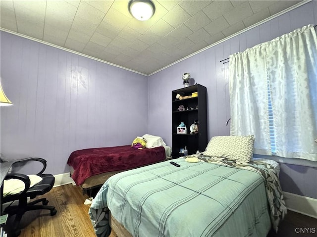 bedroom featuring baseboards, wood finished floors, and crown molding