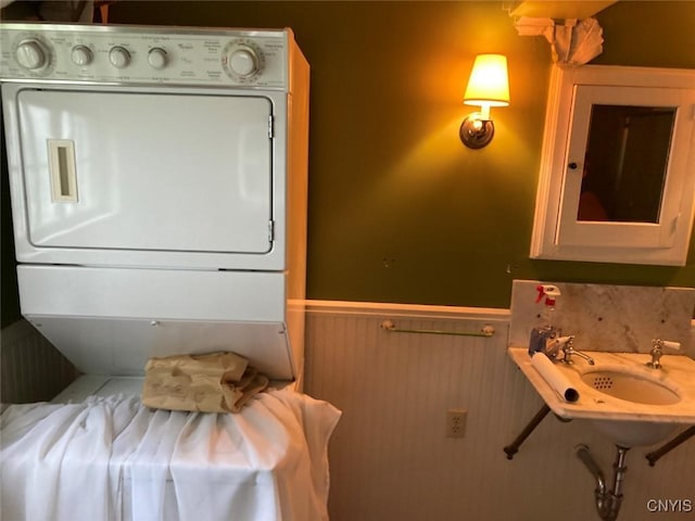 bathroom featuring a wainscoted wall, a sink, and stacked washing maching and dryer