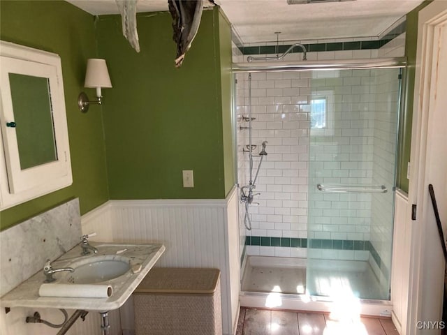 bathroom featuring tile patterned flooring, a wainscoted wall, a stall shower, and a sink