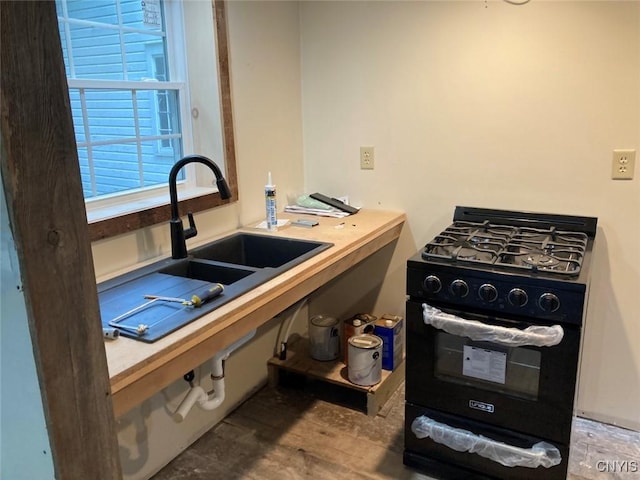kitchen with light countertops, wood finished floors, a sink, and black range with gas cooktop