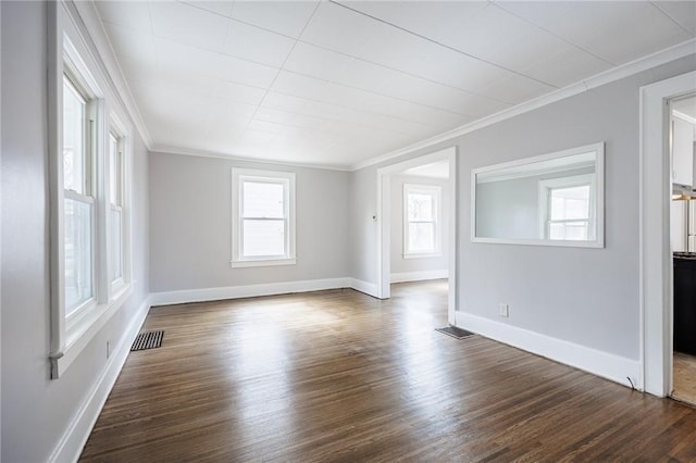 empty room featuring crown molding, dark wood-style flooring, baseboards, and visible vents
