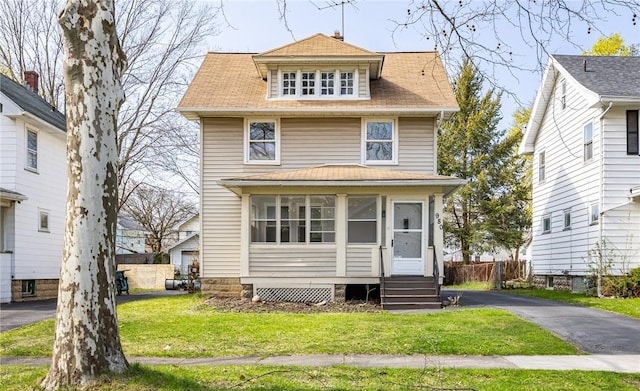 american foursquare style home with entry steps, a front yard, a sunroom, and roof with shingles