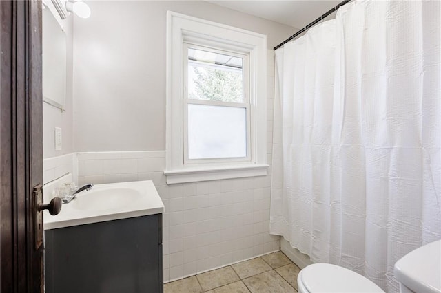 full bath featuring tile patterned floors, tile walls, toilet, vanity, and curtained shower