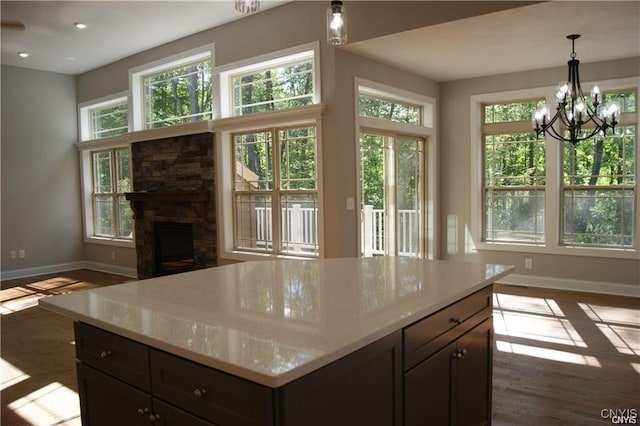 kitchen featuring baseboards, pendant lighting, a stone fireplace, and wood finished floors