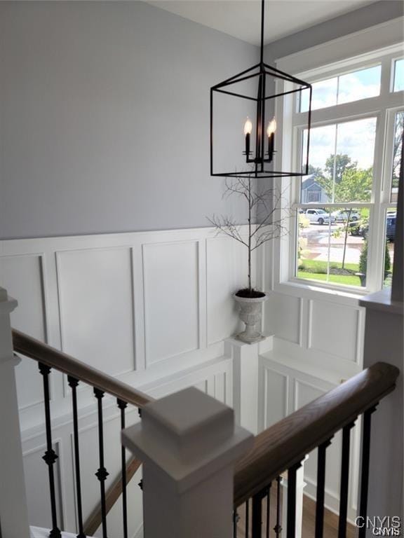 stairway featuring an inviting chandelier, a wealth of natural light, a decorative wall, and a wainscoted wall
