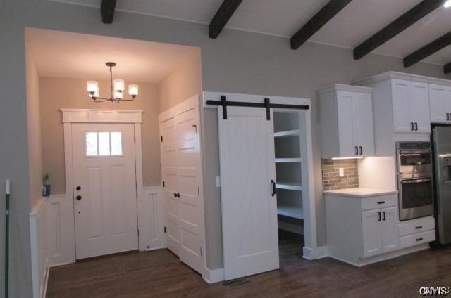 foyer entrance featuring dark wood-type flooring, a barn door, a chandelier, and beamed ceiling