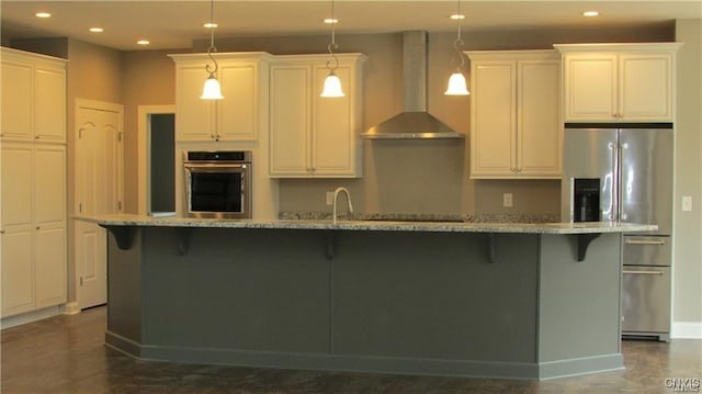 kitchen with light stone countertops, stainless steel appliances, wall chimney exhaust hood, a spacious island, and decorative light fixtures