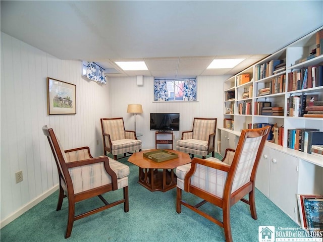 sitting room with wooden walls, a drop ceiling, and carpet floors