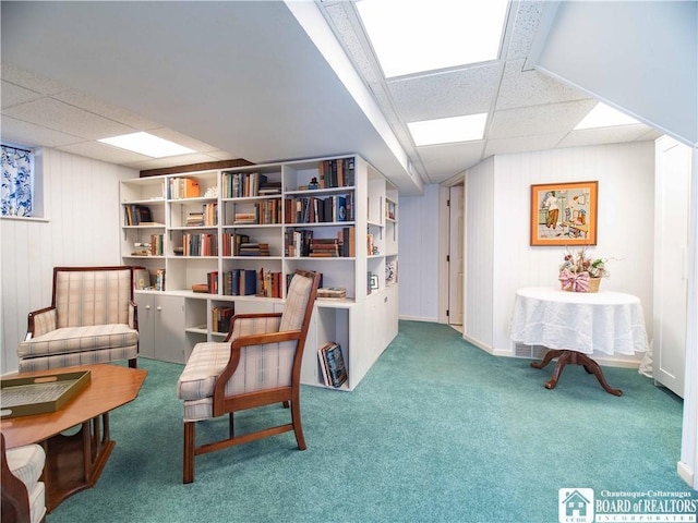living area featuring wooden walls, carpet flooring, and a paneled ceiling