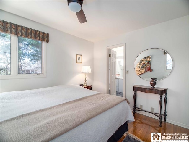 bedroom featuring baseboards, hardwood / wood-style floors, ceiling fan, and ensuite bath