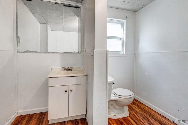 half bath featuring wood finished floors, a drop ceiling, toilet, and vanity