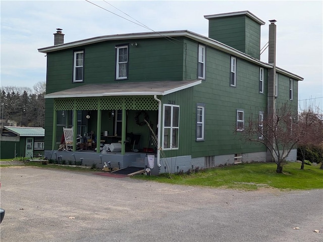 back of house with a chimney and covered porch