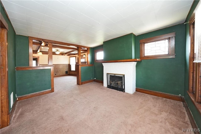 unfurnished living room featuring a brick fireplace, ceiling fan, carpet, and a healthy amount of sunlight