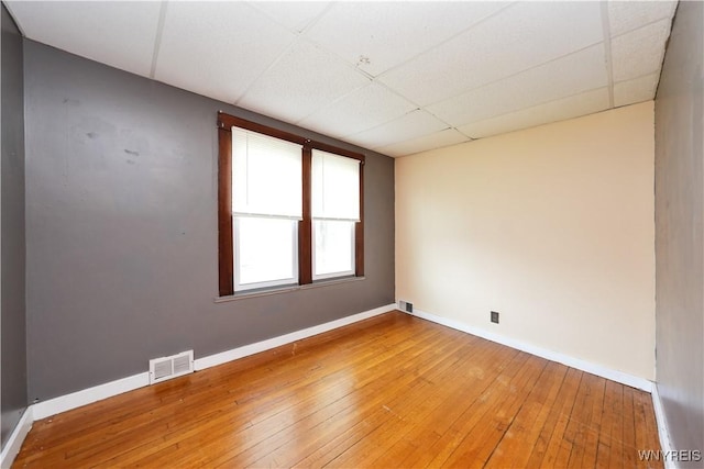 unfurnished room with baseboards, visible vents, light wood-type flooring, and a drop ceiling