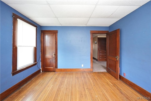 unfurnished bedroom featuring baseboards, light wood-style floors, and a drop ceiling