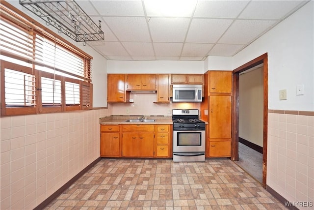 kitchen with tile walls, a sink, a paneled ceiling, stainless steel appliances, and light countertops