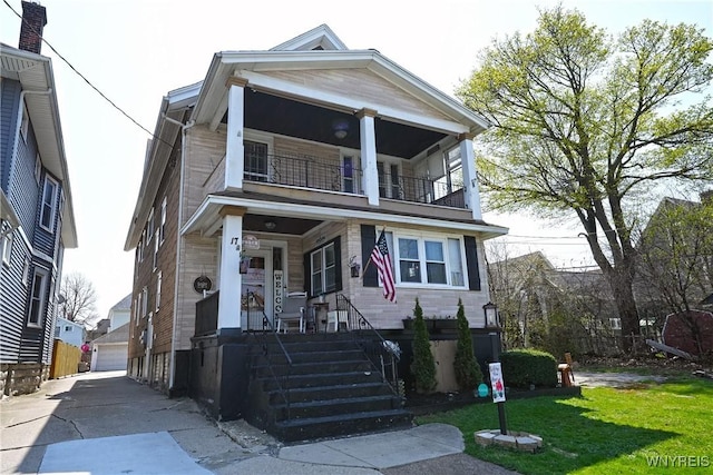 view of front of home with a porch, an outbuilding, a detached garage, a balcony, and a front yard