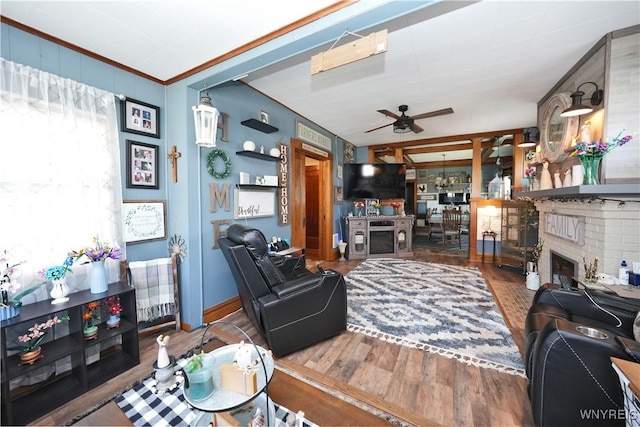 living room featuring wood finished floors, ornamental molding, ceiling fan, a fireplace, and baseboards