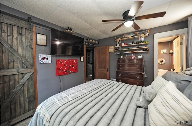 bedroom with a barn door, a ceiling fan, and ensuite bath