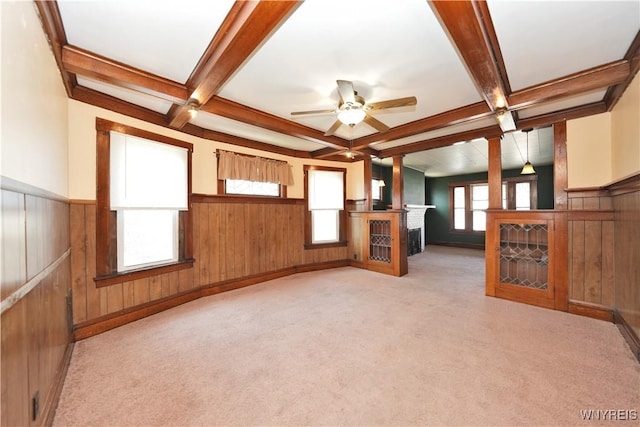 unfurnished living room with coffered ceiling, light colored carpet, beamed ceiling, a wainscoted wall, and a ceiling fan