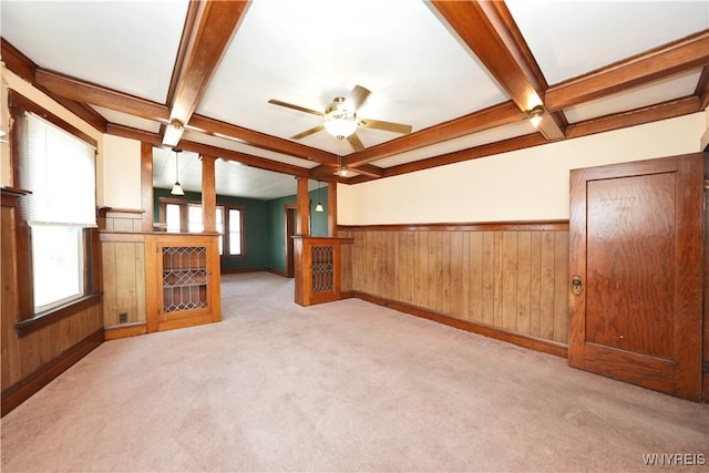 unfurnished living room with coffered ceiling, beamed ceiling, carpet, a wainscoted wall, and a ceiling fan