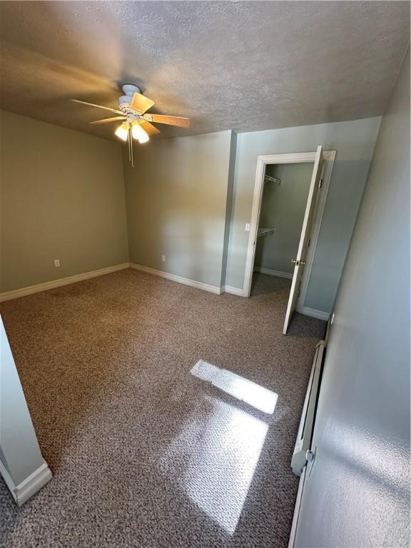 carpeted spare room featuring a textured ceiling, a ceiling fan, and baseboards