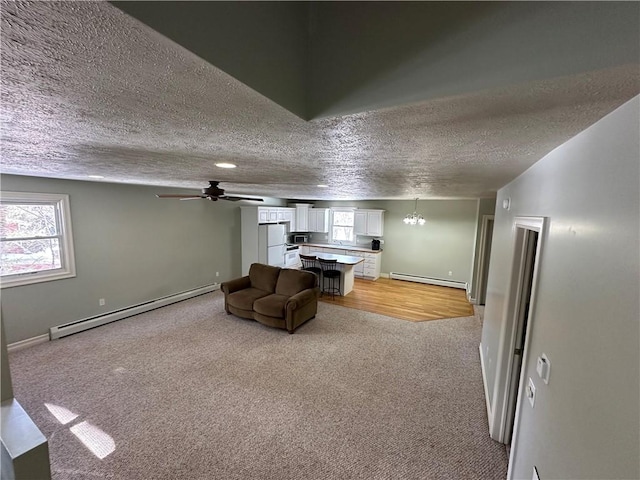 unfurnished living room with baseboard heating, baseboards, light carpet, and a textured ceiling