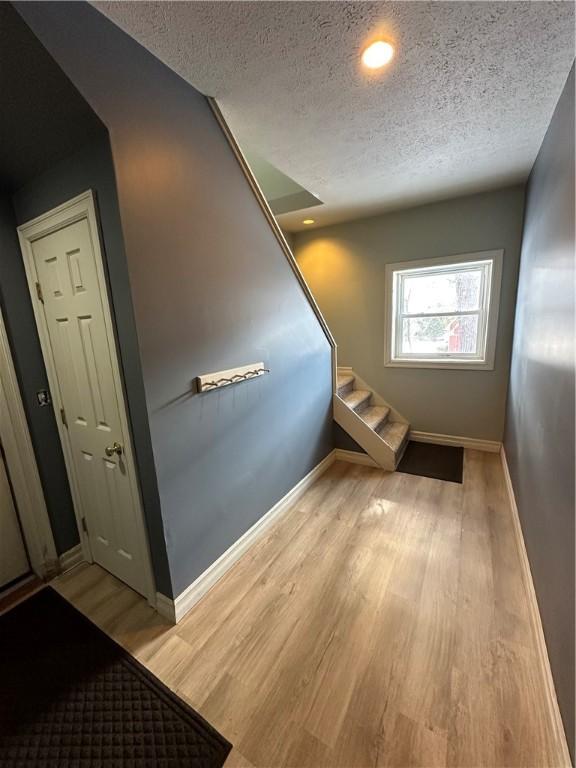 stairs featuring a textured ceiling, wood finished floors, and baseboards