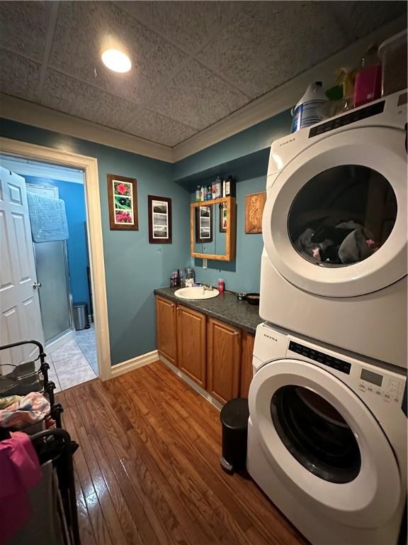 laundry area with a sink, stacked washer / drying machine, hardwood / wood-style floors, and baseboards
