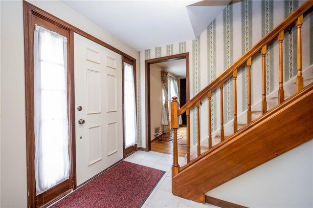 tiled entryway with stairs, wallpapered walls, and a healthy amount of sunlight