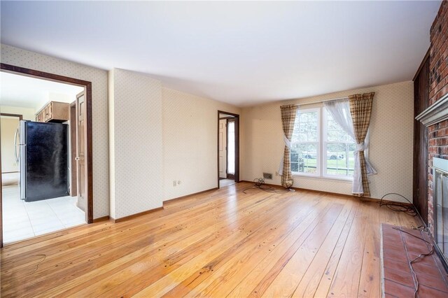 unfurnished living room featuring a fireplace, light wood-style floors, wallpapered walls, and baseboards