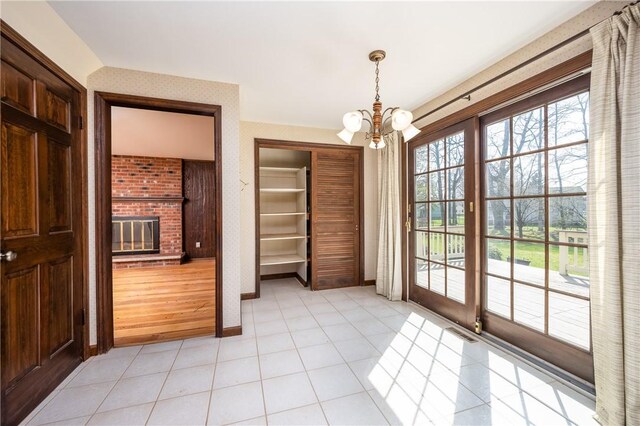 unfurnished dining area with visible vents, baseboards, light tile patterned flooring, a fireplace, and a notable chandelier