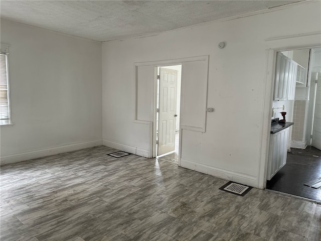 empty room with a textured ceiling, visible vents, baseboards, and dark wood finished floors