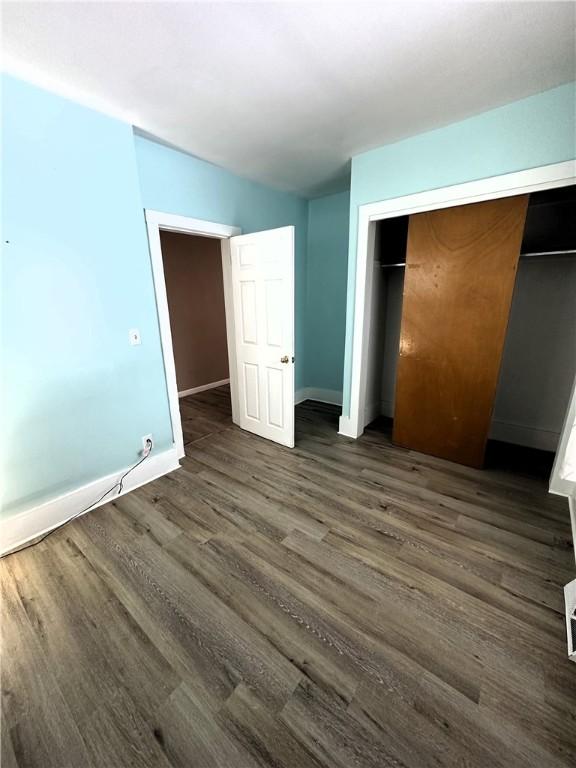 unfurnished bedroom featuring baseboards, dark wood-style flooring, and a closet