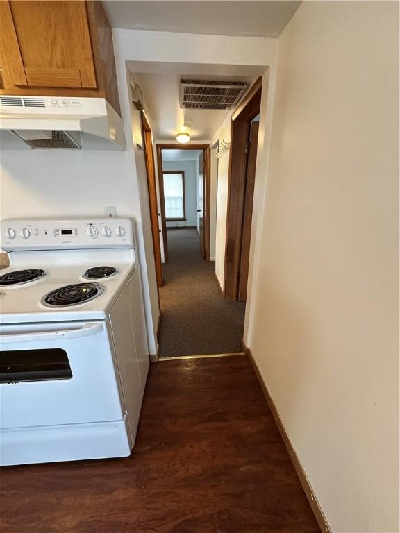 interior space with baseboards, white range with electric cooktop, under cabinet range hood, dark wood-style floors, and visible vents